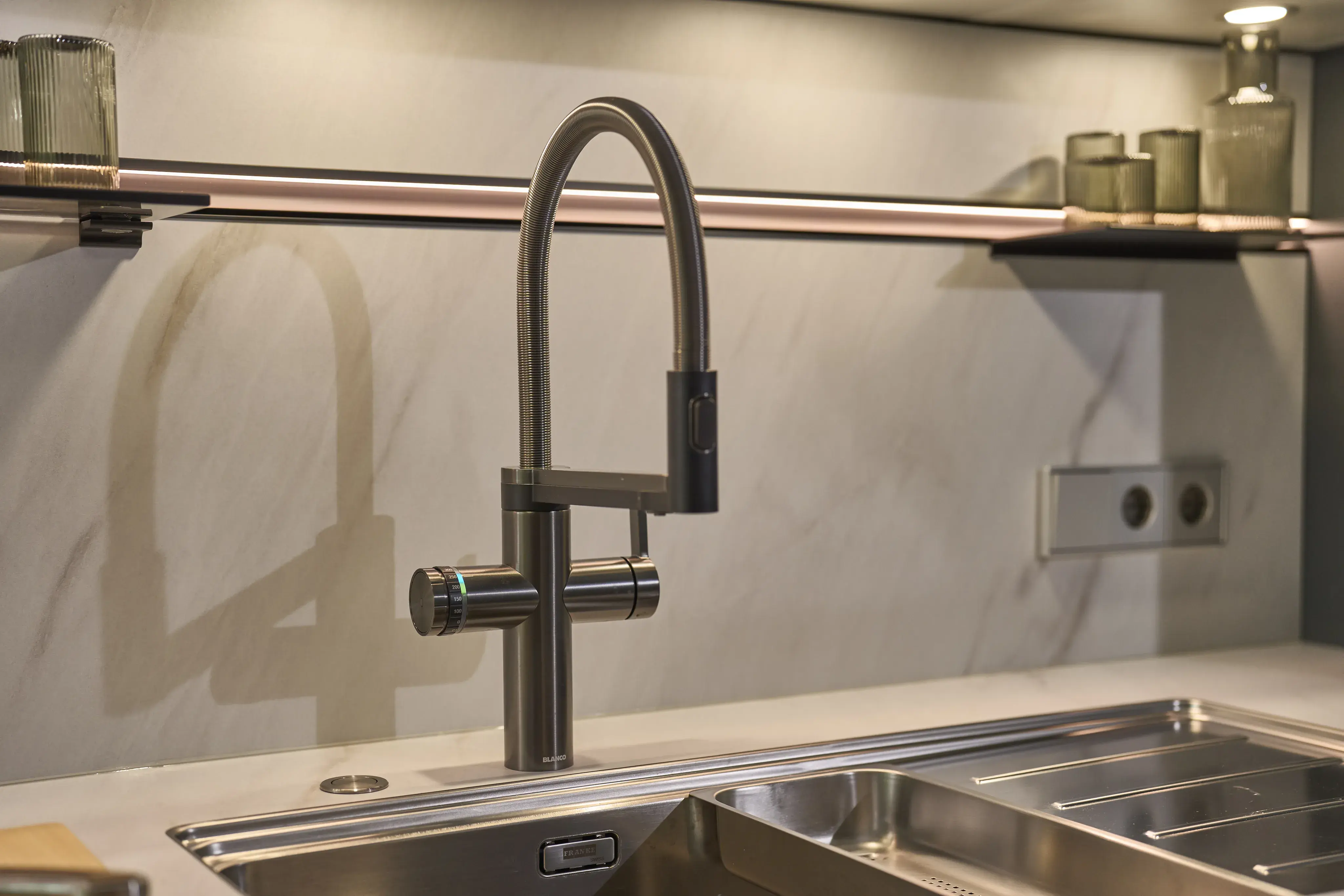 Moderne Küchenarmatur mit gebogenem Auslauf, Edelstahlspüle und schlichten Glasbehältern.