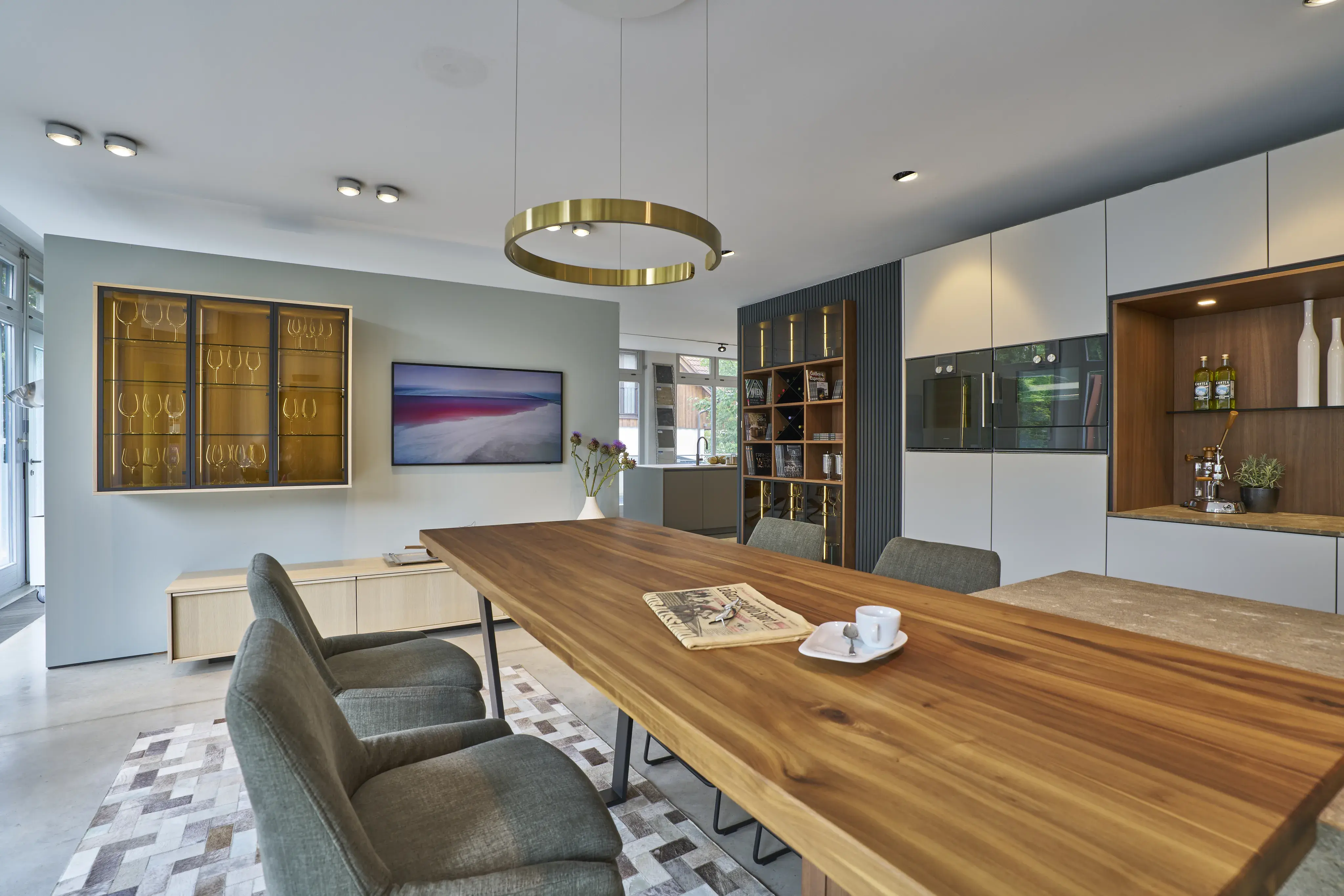 Modernes Esszimmer mit langem Holztisch, schlichten Stühlen und goldener Pendelleuchte.