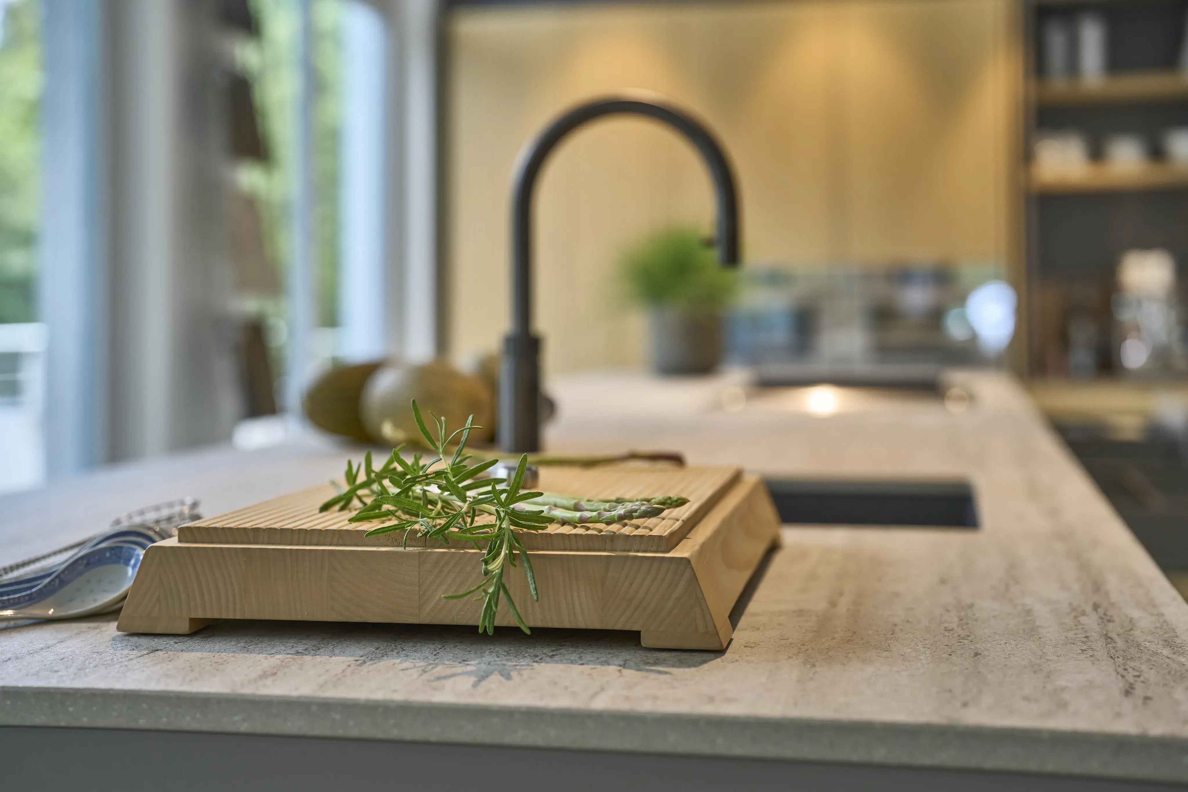 Holzbrett mit frischen Kräutern auf moderner Kücheninsel, unscharfer Hintergrund.