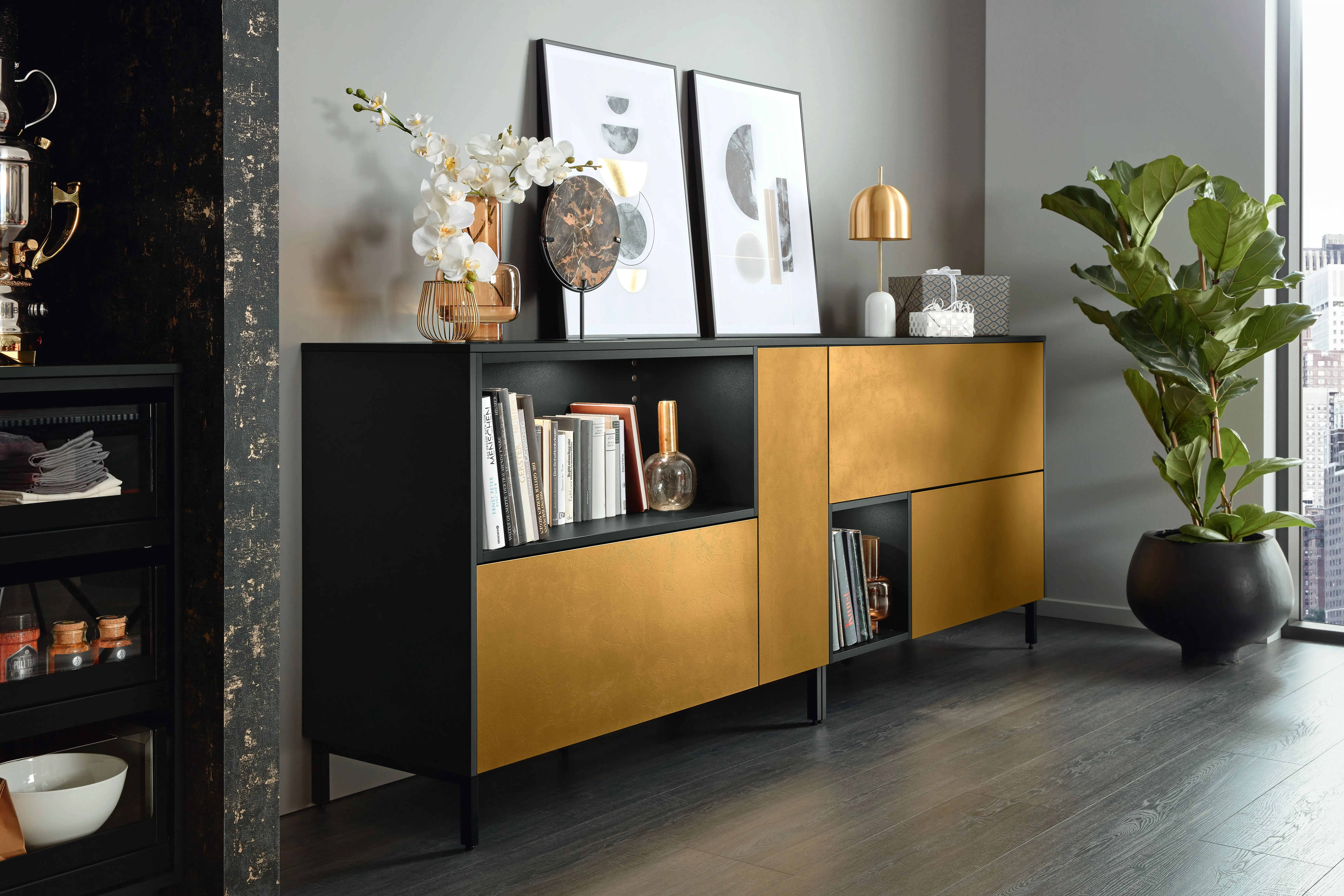 Modernes Wohnzimmer mit schwarzem und goldenem Sideboard, Pflanze und Dekorationen.
